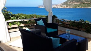 An outdoor seating area with wicker furniture and a glass table, overlooking a coastal landscape. - Sea Vessel (Mylopotamos)