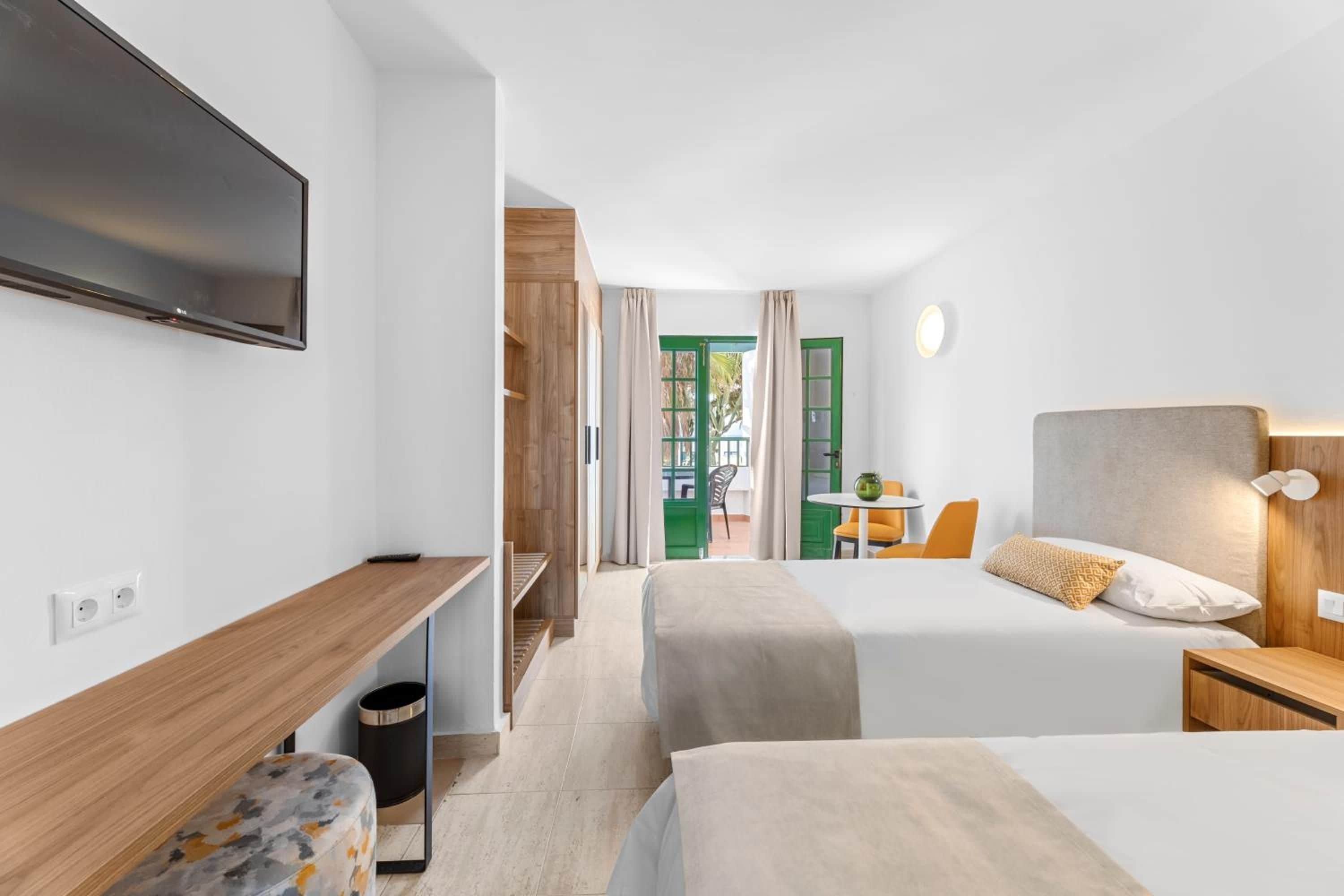 Habitación de hotel con dos camas, un escritorio, televisión y vistas al exterior.