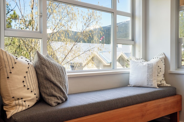 A window seat with cushions, a view of a mountain, and a building with a red and white flag.