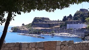 A coastal view with a fortified structure, a marina with boats, and a prominent building with a cross. - Corfu-town Apartment best location/2BR/lift/removed/smart<br>TV+Netflix.<br>  (Kerkira)