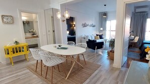 A modern living room with a round dining table, white chairs, a yellow cabinet, and a large window with curtains. - Corfu-town Apartment best location/2BR/lift/removed/smart<br>TV+Netflix.<br>  (Kerkira)