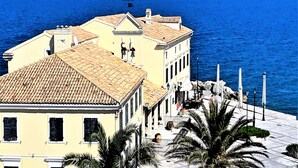 A coastal building with a tiled roof, a balcony, and a view of the sea. - Corfu-town Apartment best location/2BR/lift/removed/smart<br>TV+Netflix.<br>  (Kerkira)