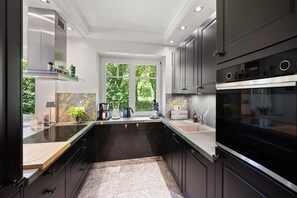 A modern kitchen with a large island, built-in appliances, and a view of greenery outside.