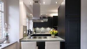 A modern kitchen with dark cabinets, a central island with two white chairs, and a window on the left. - 5***** Luxury pool villa, very quiet location, free WLAN, heated pool, 3000 sqm  (Boltenhagen)