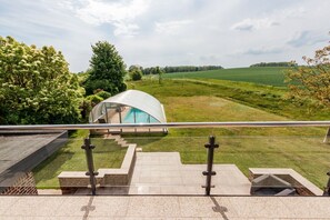 Une maison moderne dotée d’une véranda en verre, d’une piscine et offrant une vue sur un champ verdoyant.