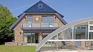 A swimming pool with a clear blue water surface, surrounded by a wooden deck. In the background, there is a two-story house with a brick facade and large windows. - 5***** Luxury pool villa, very quiet location, free WLAN, heated pool, 3000 sqm  (Boltenhagen)