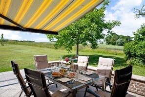 Un espace de restauration en plein air avec une table dressée pour quatre personnes, entourée de chaises en osier, sous une marquise à rayures.