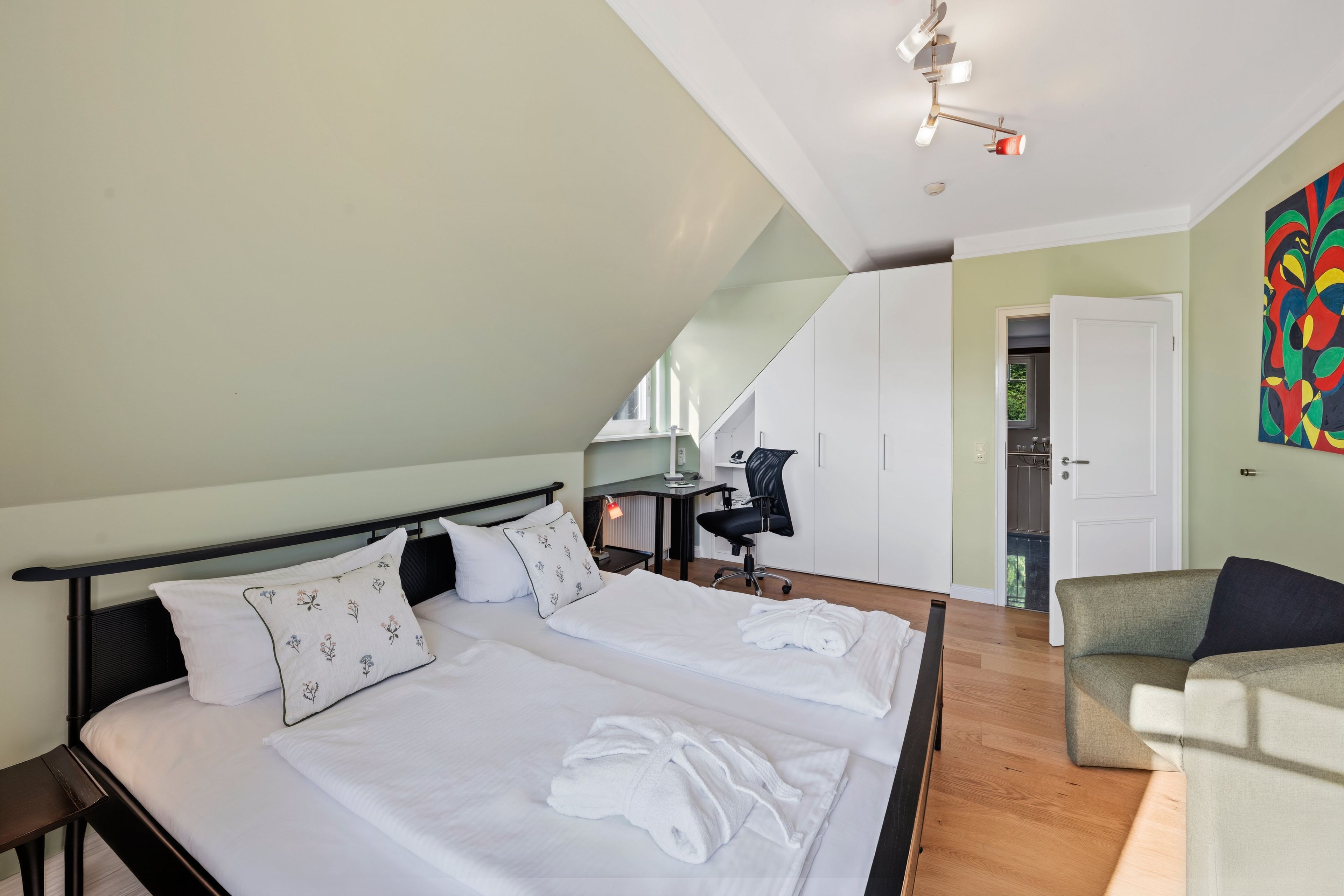Een slaapkamer met een bed, een bureau, een stoel en een kleurrijk abstract schilderij aan de muur.