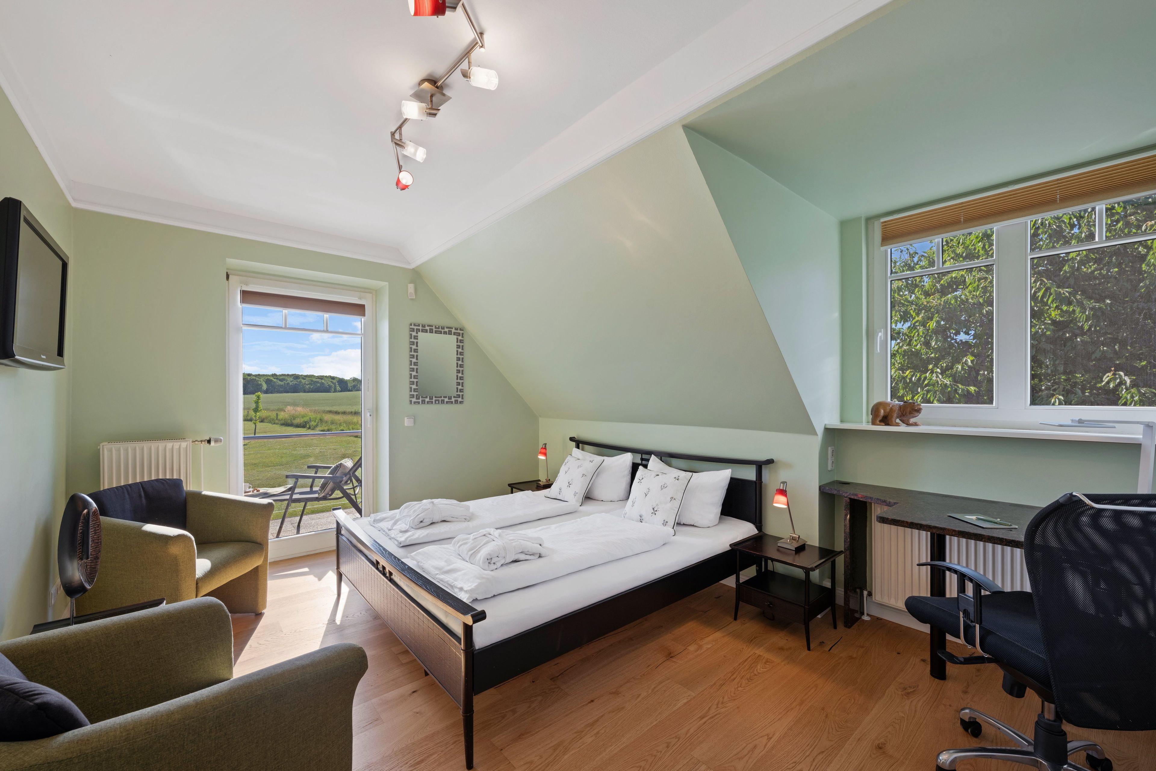 Een slaapkamer met een bed, een bureau, een stoel en uitzicht op het groen.