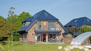 A two-story house with a brick exterior, large windows, and a covered outdoor seating area. - 5***** Luxury pool villa, very quiet location, free WLAN, heated pool, 3000 sqm  (Boltenhagen)