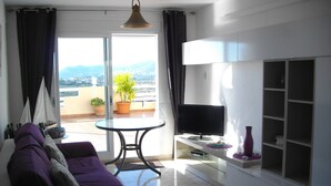 A modern living room with a sofa, a TV, a balcony with a potted plant, and a view of the mountains. - panoramic terrace air-conditioned apartment 2 bedrooms 4 pers (Peñíscola)