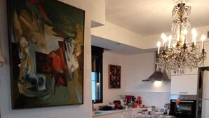 A dining area with a long table set for six, a chandelier, and a large abstract painting on the wall. - Beautiful 1 Bedroom in New GINDI Complex (Tel Aviv-Yafo)