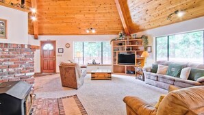 Una sala acogedora con chimenea de ladrillo, techo de madera y ventanas amplias.