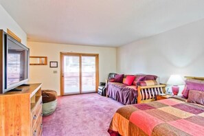 Un dormitorio con una cama grande, televisión, cómoda de madera y puerta corrediza de vidrio que da a un área exterior.