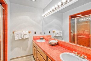 Un baño con dos lavamanos, un espejo grande con luces, y toallas colgadas en ganchos.