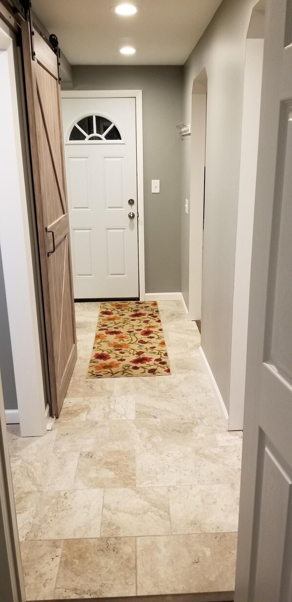 A hallway with a patterned rug, a white door with a semi-circular window, and a light switch on the wall.