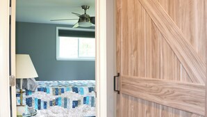 Ein Schlafzimmer mit Bett, Deckenventilator, Fenster und Holztür.