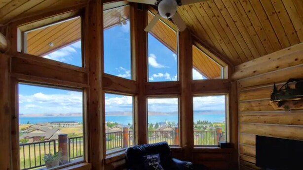 A log cabin interior with a large window offering a view of a residential area and a body of water. - Fantastic view! Arcade, Jacuzzi, Family Friendly Cottage! (Garden City)