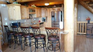 A rustic kitchen with wooden cabinets, a stainless steel refrigerator, and a bar area with stools. - Fantastic view! Arcade, Jacuzzi, Family Friendly Cottage! (Garden City)