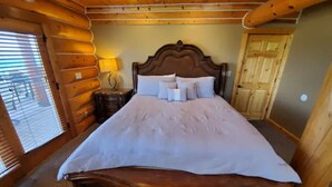A wooden log cabin-style bedroom with a large bed, a nightstand, and a lamp. - Fantastic view! Arcade, Jacuzzi, Family Friendly Cottage! (Garden City)