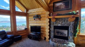 A log cabin interior with a stone fireplace, a television, and a leather couch. - Fantastic view! Arcade, Jacuzzi, Family Friendly Cottage! (Garden City)