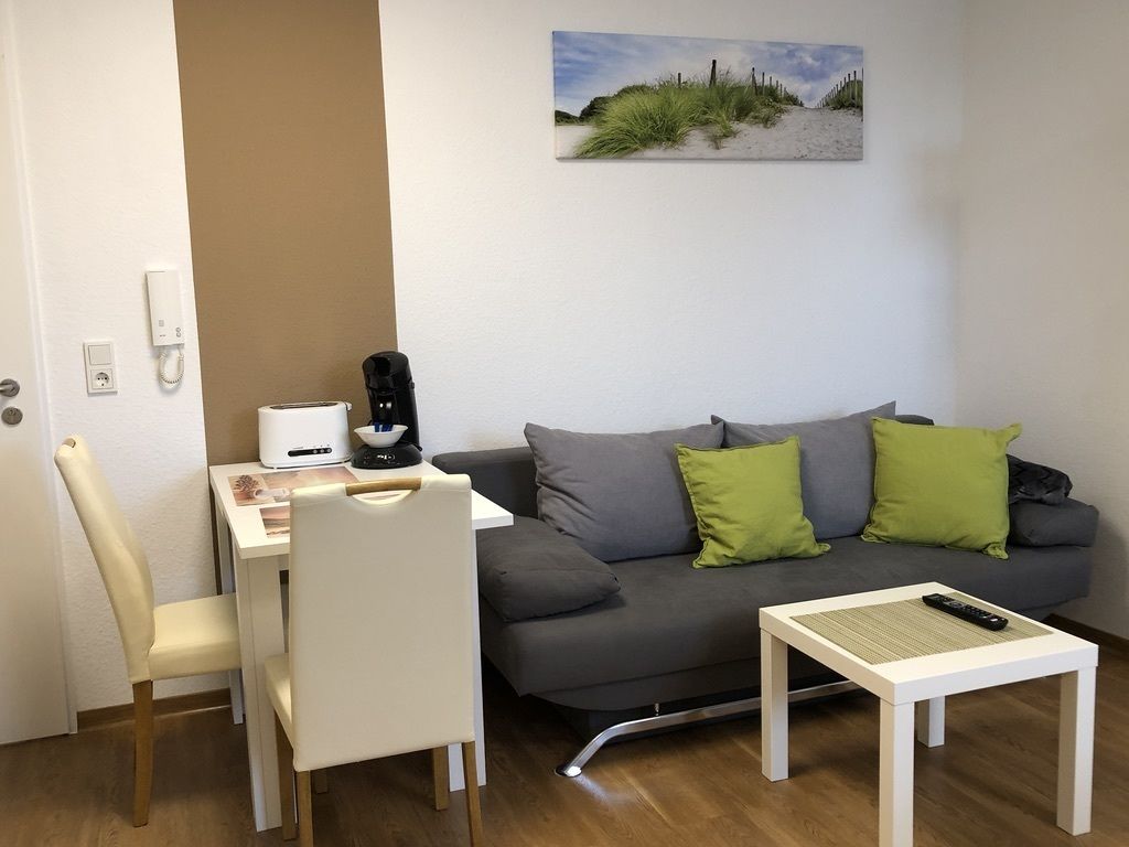 A modern living room with a grey sofa, two green cushions, a white coffee table, and a white chair.