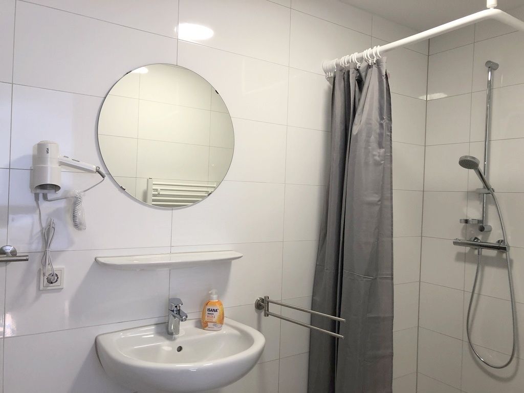 Un baño con lavamanos, espejo, ducha y toallero.