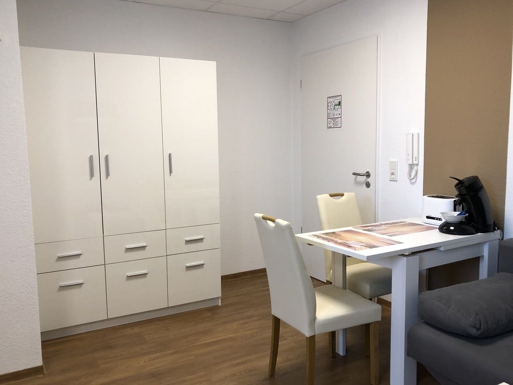 Une pièce comprenant une armoire blanche, une table à manger avec des chaises, une machine à café et un canapé.