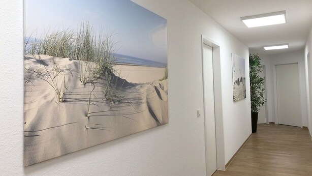 Een gang met een groot schilderij van een strand, een potplant en een deur aan het einde.