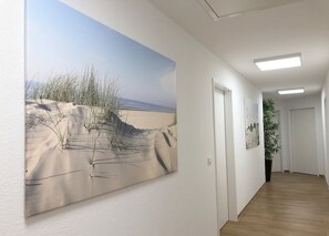A hallway with a large painting of a beach scene, a potted plant, and a door at the end. - Fewo und Meer Whv (Wilhelmshaven)