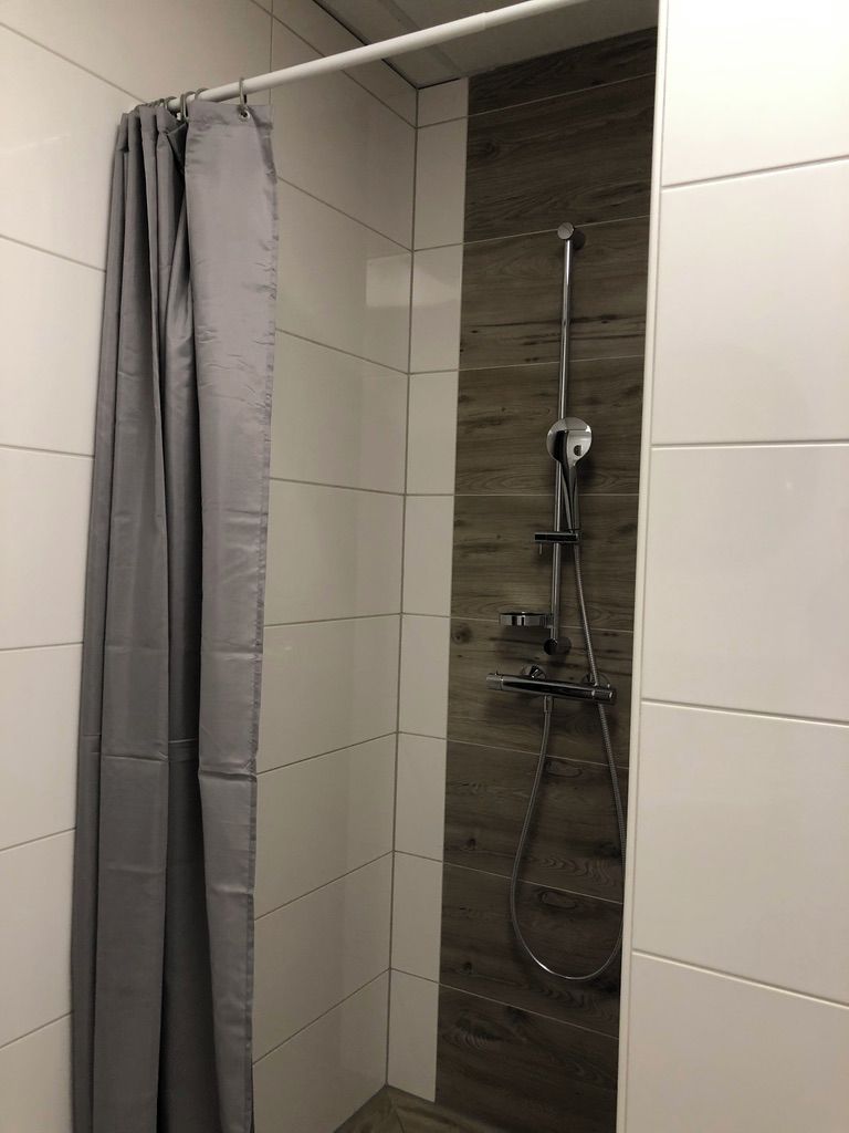 A shower area with a grey shower curtain, a wooden panel wall, and a chrome showerhead.