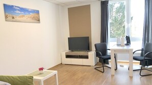 Een moderne woonkamer met een flatscreen televisie, twee zwarte stoelen, een klein tafeltje met een vaas en een bank.