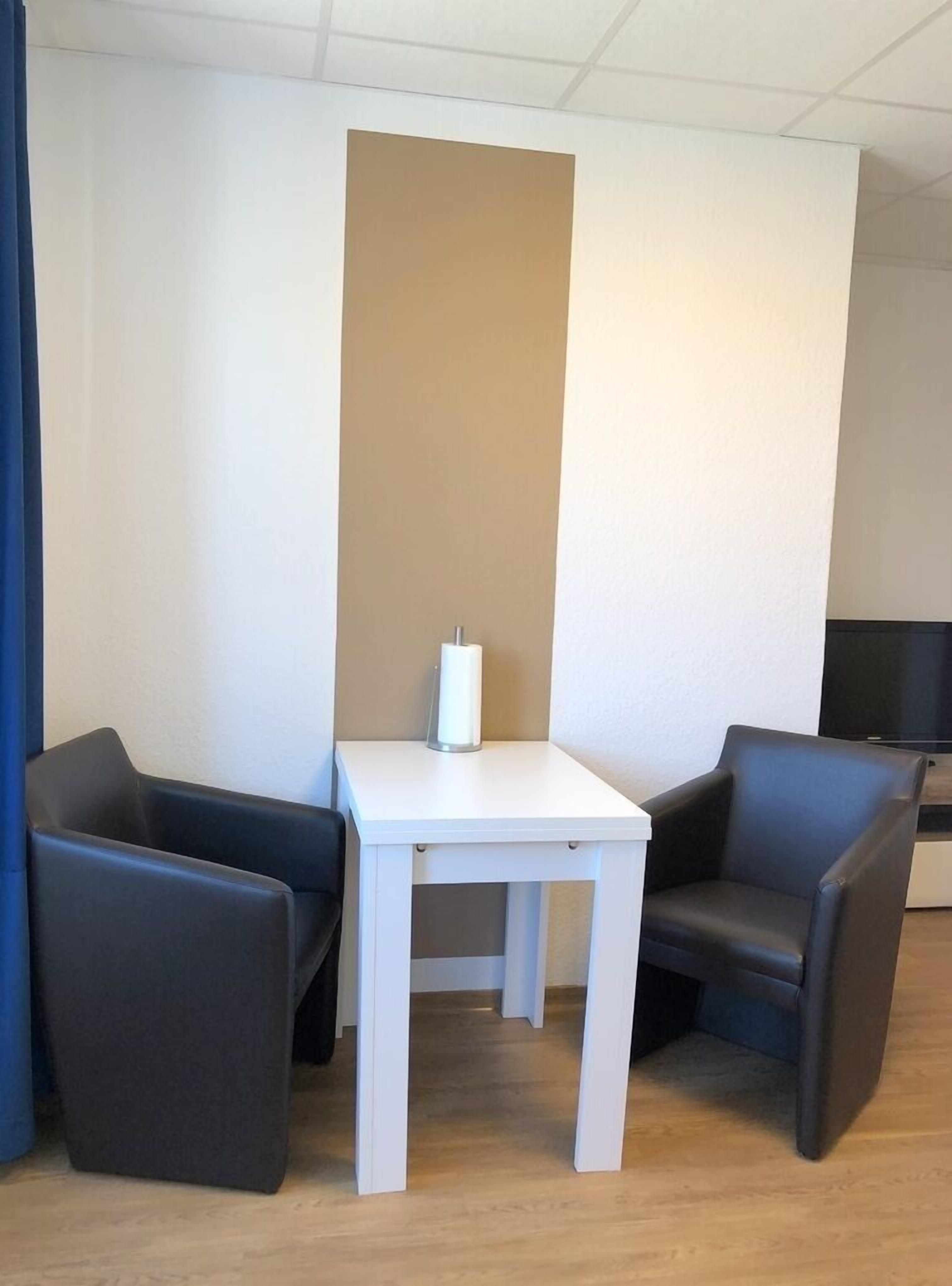 A room with a white table and two black chairs, a blue curtain, and a beige wall.