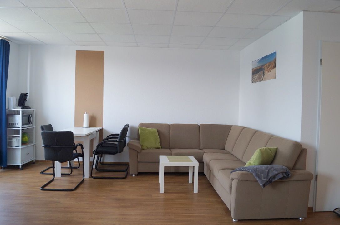 Una sala moderna con un sofá color beige, una mesita blanca y una silla negra.