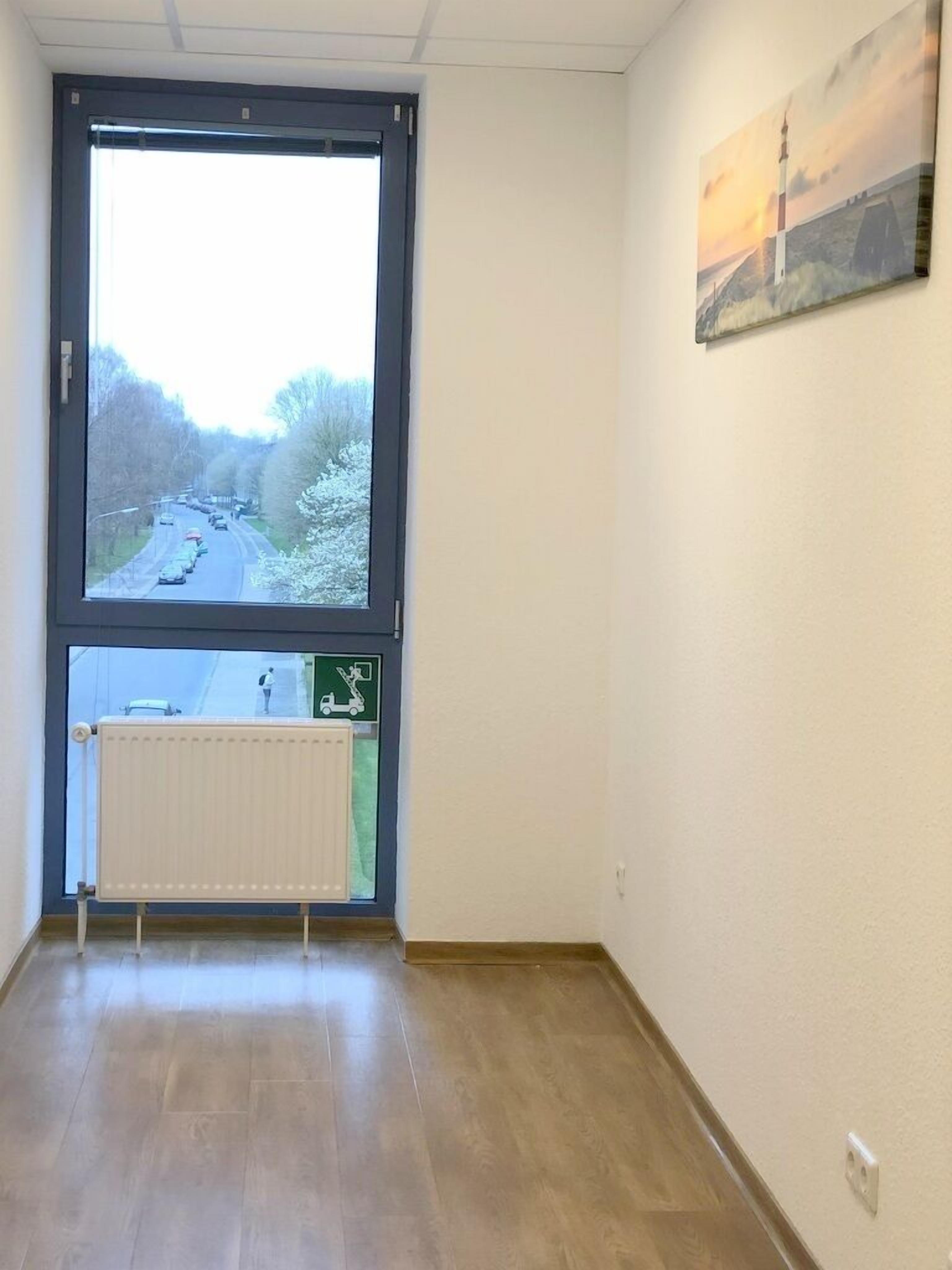 Een kamer met een groot raam, een radiator en een schilderij aan de muur.