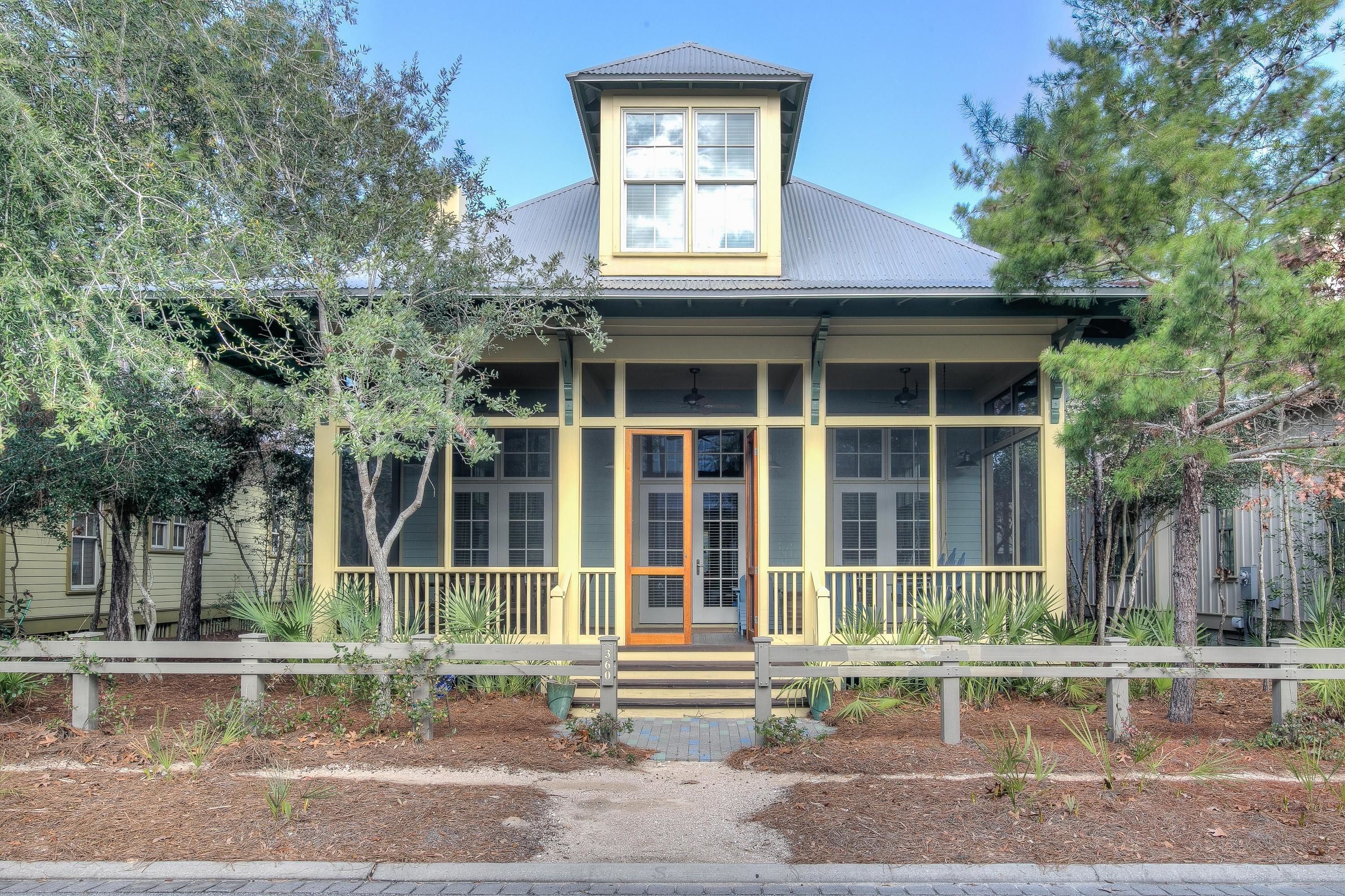 A two-story building with a prominent front porch, large windows, and a small tower-like structure on the roof.