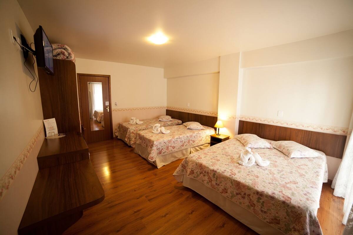 A hotel room with two beds, wooden flooring, a desk, a TV, and a mirror.