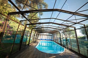 A glass-enclosed swimming pool with a wooden deck and metal railings. - Pousada Vollweiter (Guarapuava)