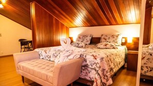 Ein Schlafzimmer mit Holzbalkendecke, einem Bett mit floralem Bettbezug, einem rosafarbenen Sessel und einem kleinen Tisch.