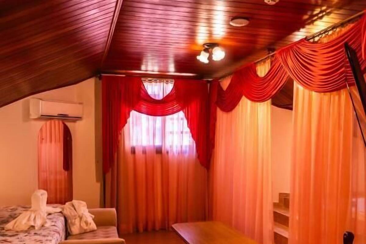 A cozy room with a wooden ceiling, a bed with a floral bedspread, a small table, and a chair.