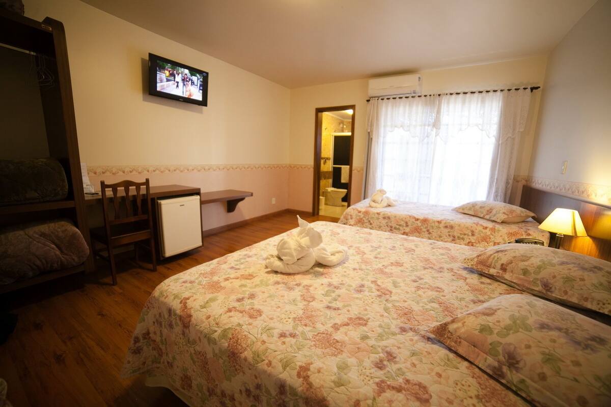 A hotel room with two beds, a small desk, a chair, a television, and a bathroom visible through an open door.
