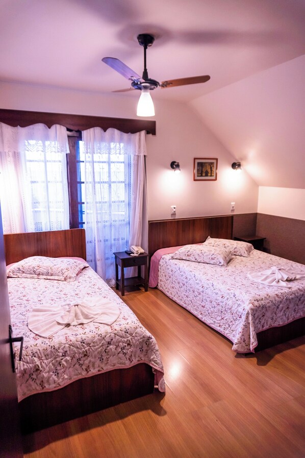 Una habitación con dos camas, ventilador de techo, mesita de noche y una ventana con cortinas.