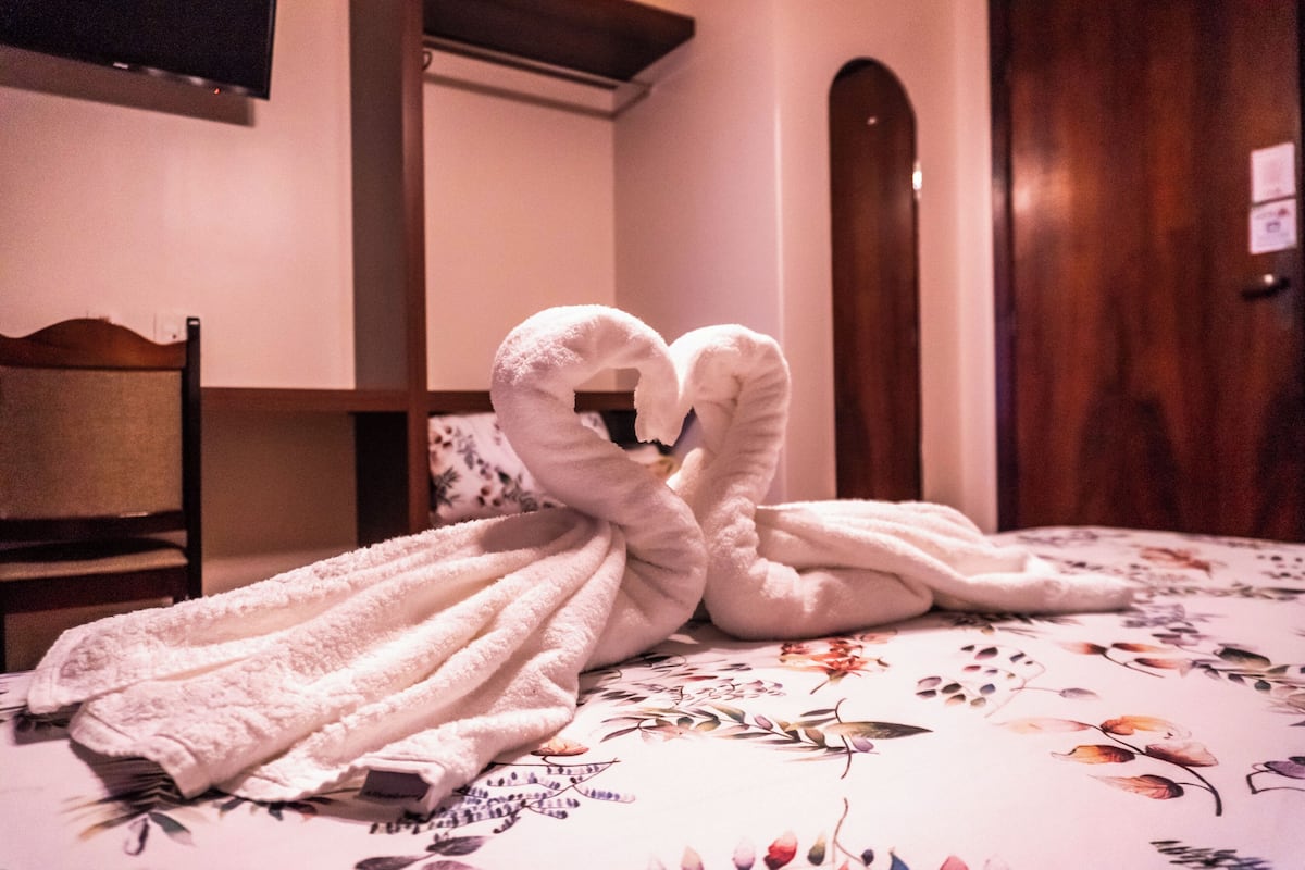 A bed with floral bedding and a heart-shaped towel arrangement.
