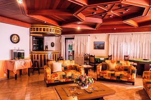 Uma sala de estar acolhedora com dois sofás, uma mesa de centro com arranjo floral, área de bar e mesa de jantar.