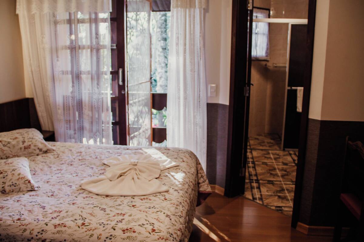 A bedroom with a floral bedspread, a white towel on the bed, and a view through a door to a balcony.