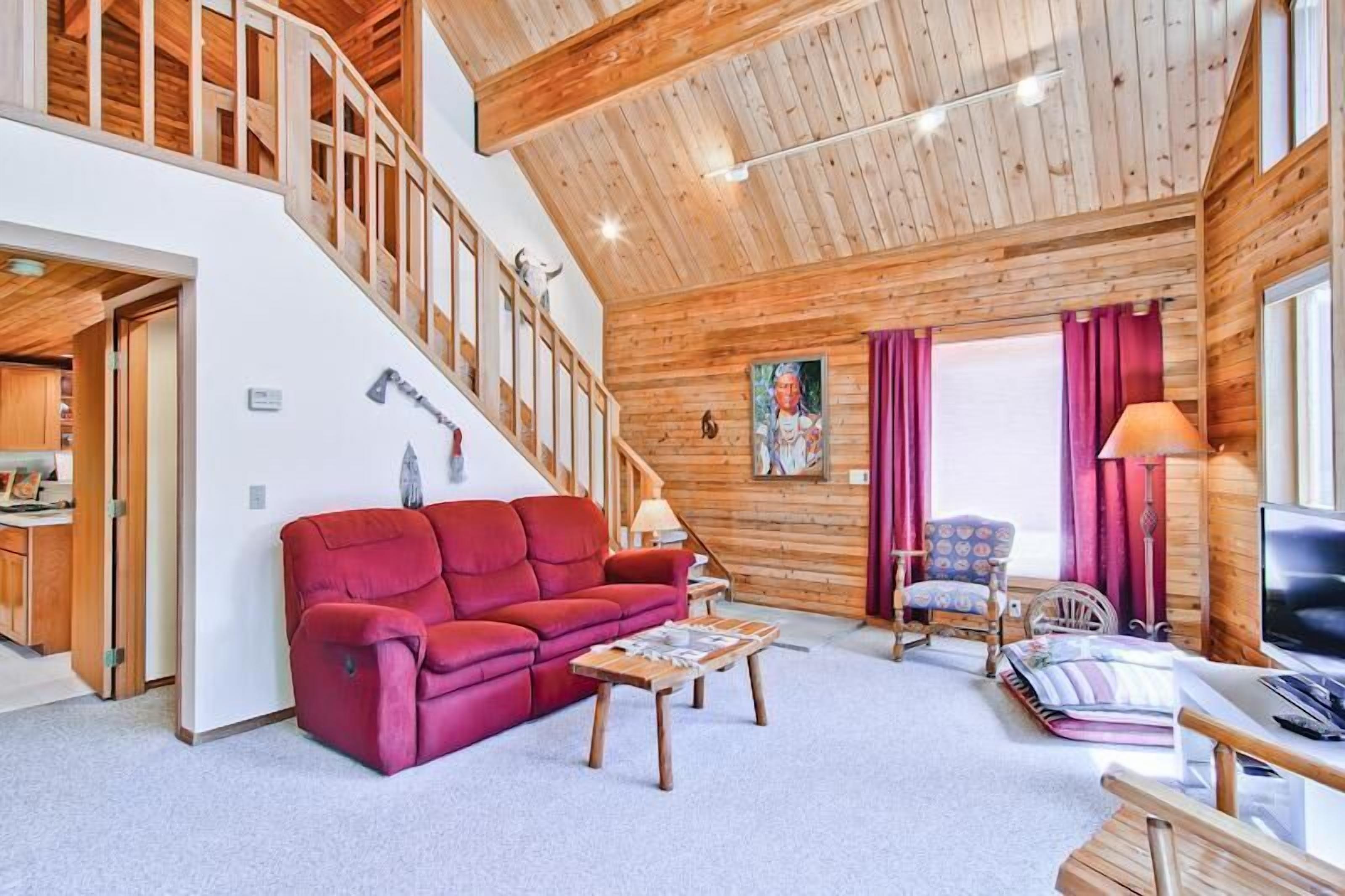 A spacious living area with a red sofa, wooden flooring, a staircase, and a television.