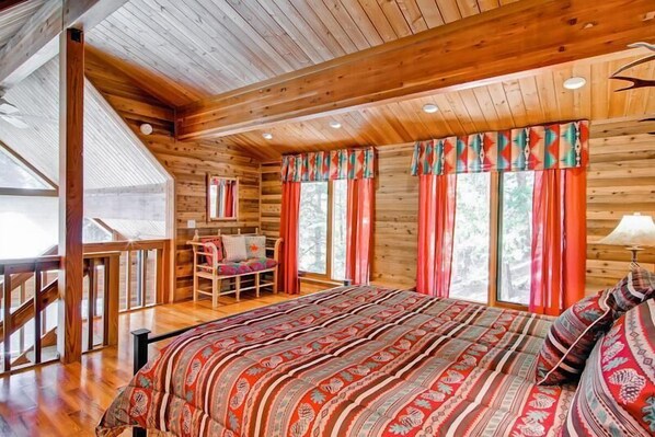 Une chambre dans une cabane en bois, avec un grand lit, une chaise en bois et une fenêtre avec des rideaux.