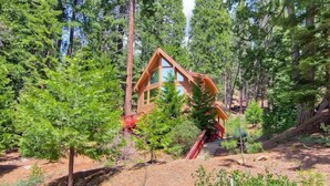 A wooden cabin surrounded by tall pine trees, with a staircase leading to the entrance. - Red Fox Retreat (Yosemite)