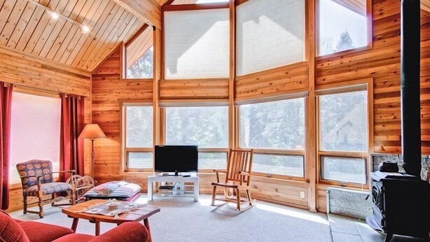 A cozy cabin interior with wooden walls, large windows, a television, a fireplace, and comfortable seating. - Red Fox Retreat (Yosemite)