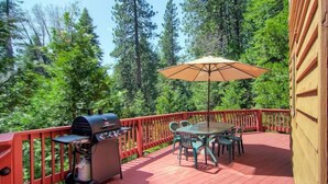 A wooden deck with a grill, outdoor table, chairs, and an umbrella. - Red Fox Retreat (Yosemite)